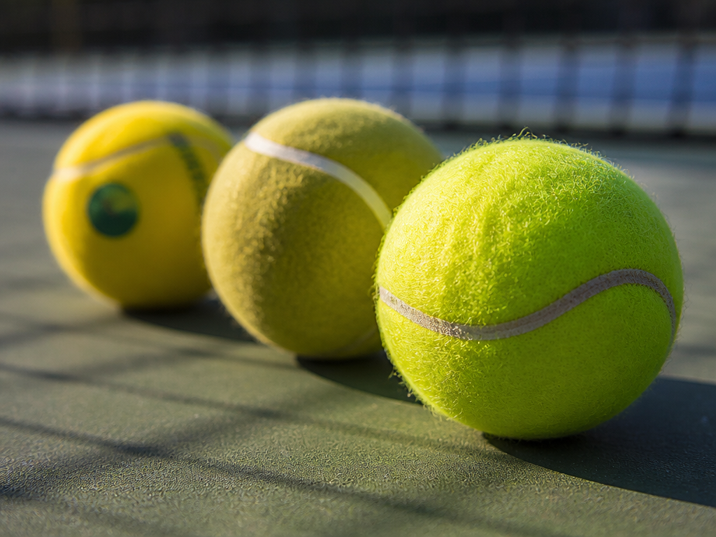 A close-up still-life photograph of three distinct types of tennis balls arranged in a…