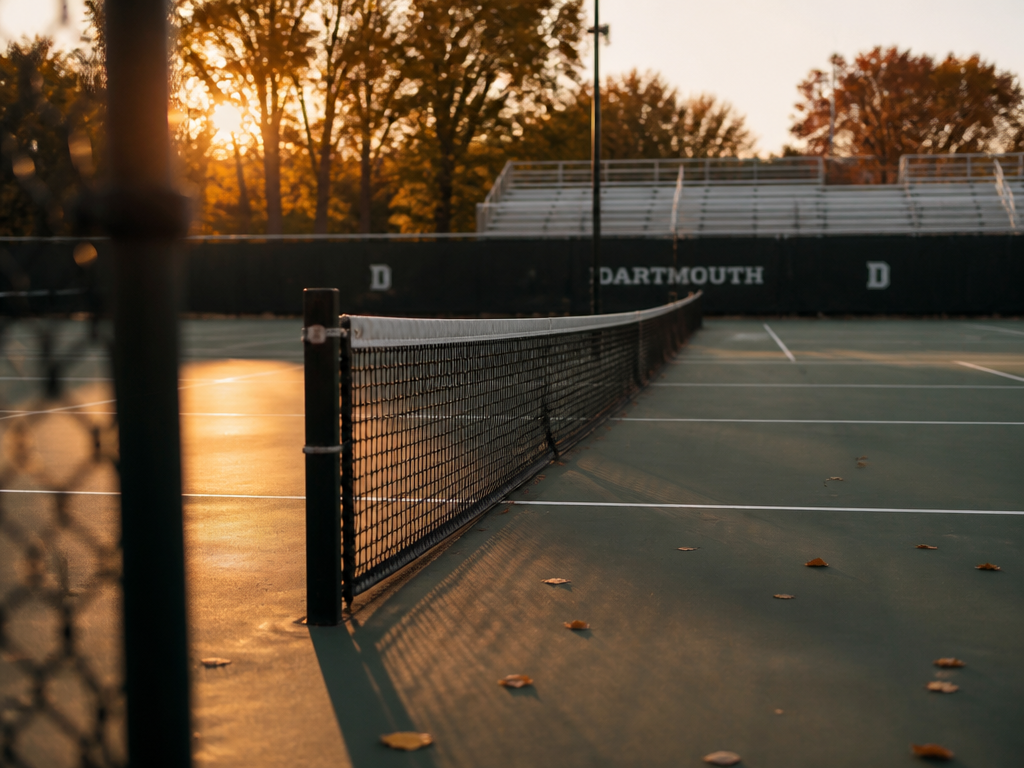 A wide, contemplative shot of an empty outdoor college tennis court at golden hour…