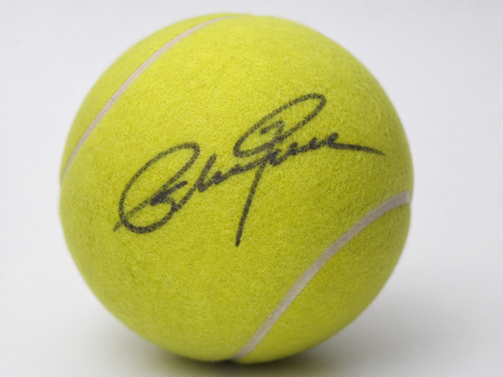 A close-up product still life of an oversized 9-inch felt tennis ball resting on…