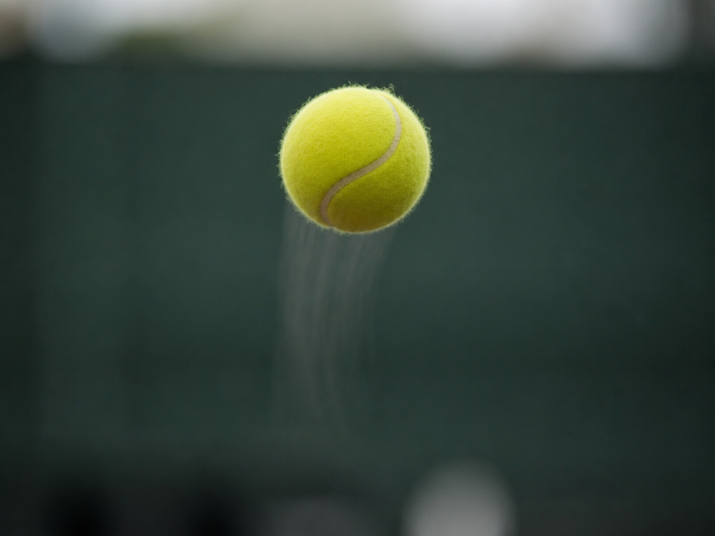 A close-up photorealistic photograph of a single yellow tennis ball suspended mid-air at the…