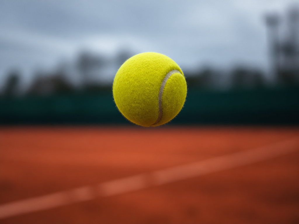 Close-up photorealistic detail of a single fluorescent yellow tennis ball suspended in mid-air at…