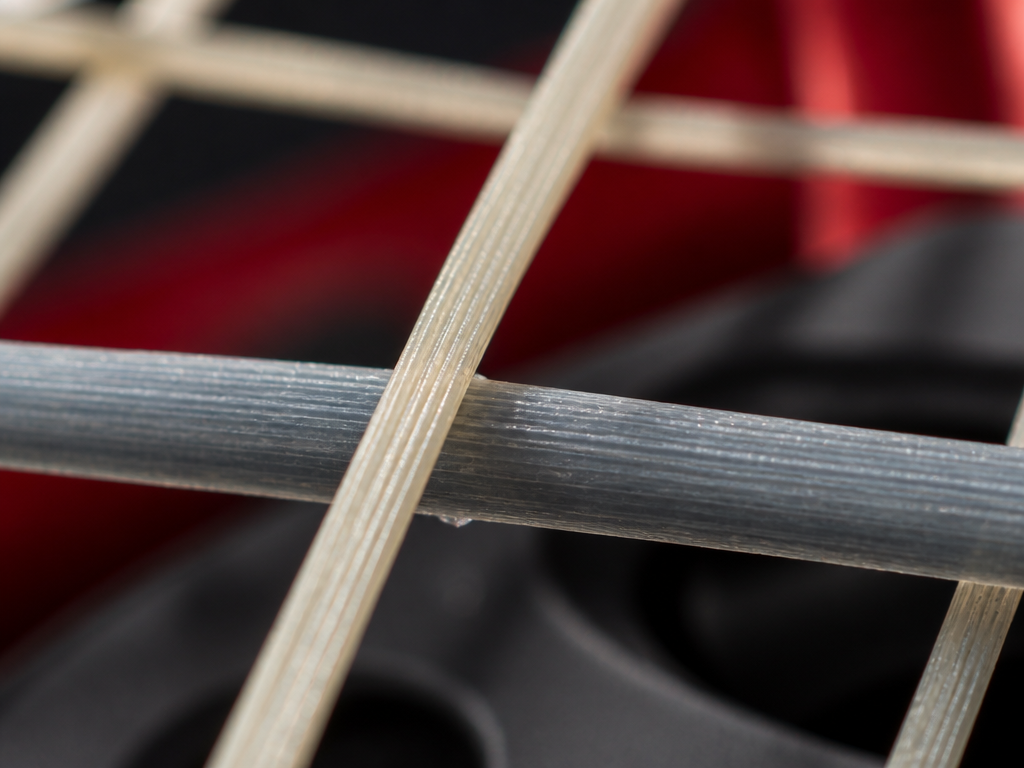 Extreme macro photograph of two tennis racquet string beds intersecting in sharp focus, one…