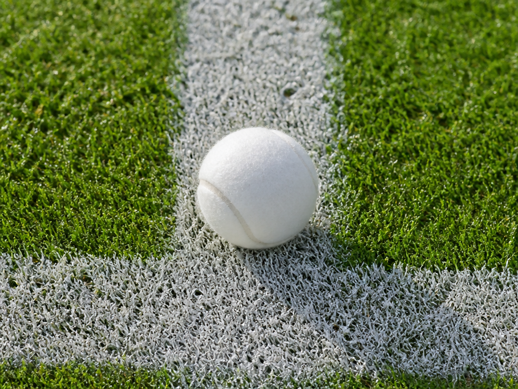 A close-up overhead photograph of a fresh white tennis ball resting on the painted…