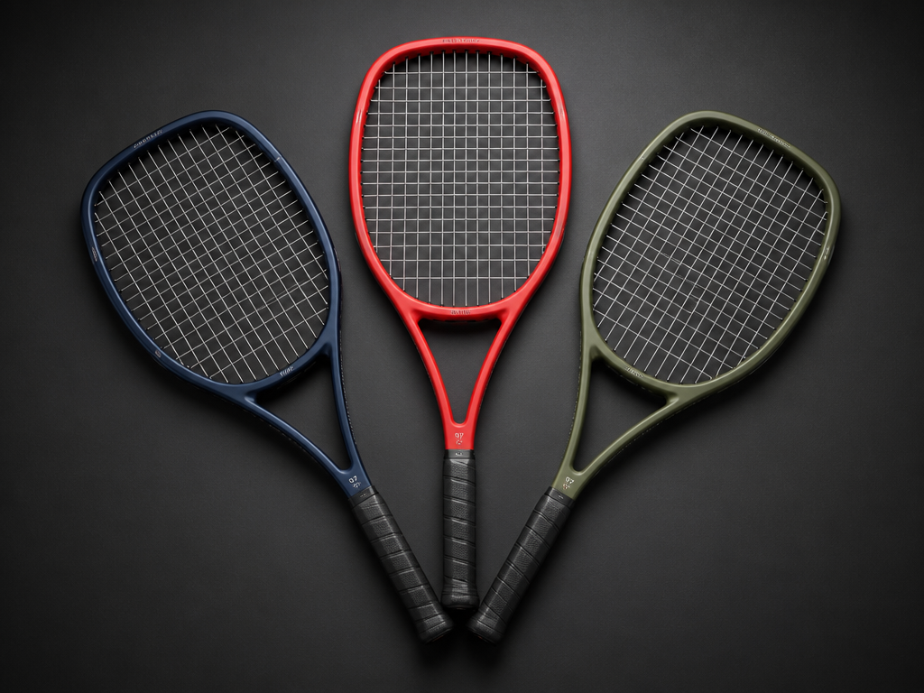 A professional studio product photograph of three tennis racquets — one deep navy blue…