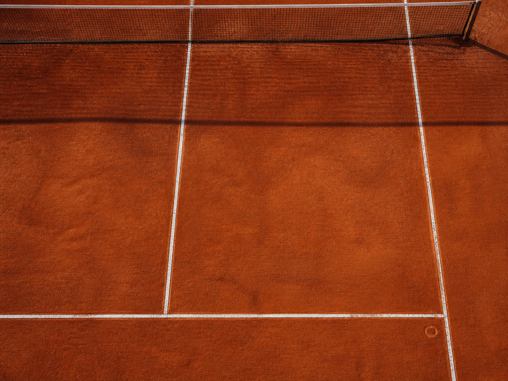An overhead top-down photograph of an empty tennis service box on a clay court…