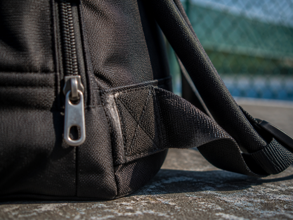 Extreme close-up product photograph of a black tennis backpack lying on a weathered concrete…