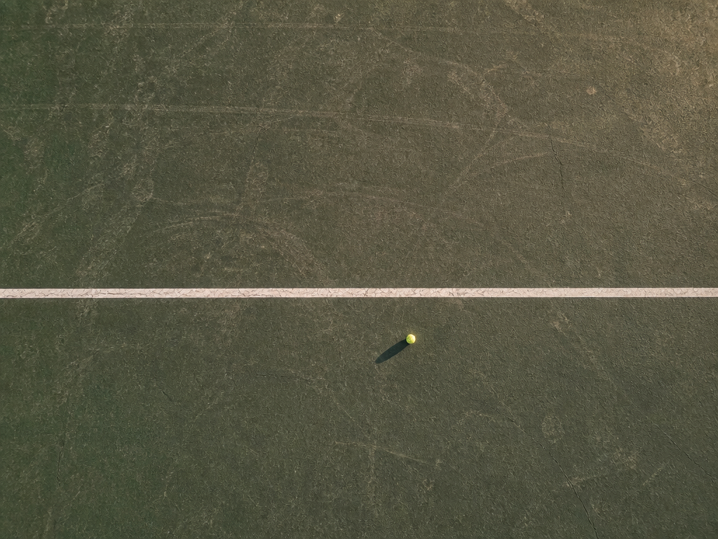 An overhead photograph of a weathered green tennis court surface photographed straight down from…
