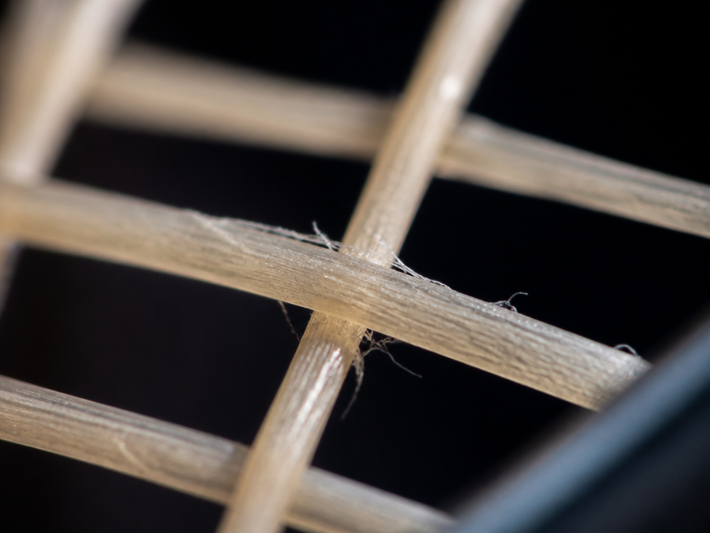 Extreme macro photograph of natural gut tennis strings woven through a racquet's string bed…