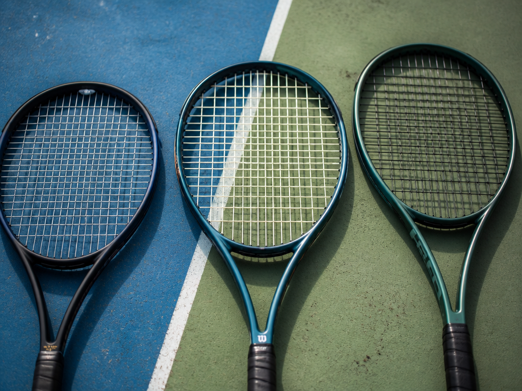 A close-up overhead flat-lay of three distinct tennis racquets arranged side by side on…